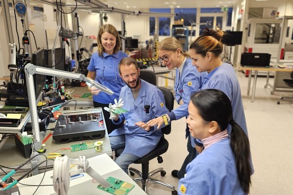 Gruppe von Mitarbeiter in ESD-Sicherheitskleidung arbeitet gemeinsam an einem Elektronik-Arbeitsplatz in Hom­brechtikon