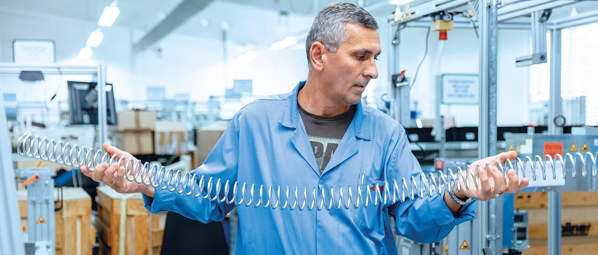 Mitarbeiter der Zollner Elektronik AG hält große Metallfeder in moderner Produktionshalle.