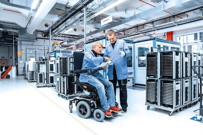 Zwei Mitarbeiter in einer Produktionshalle; Einer von ihnen sitzt im Rollstuhl