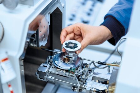 Hand platziert Probe in Rasterelektronenmikroskop für Materialanalyse mittels EDS.