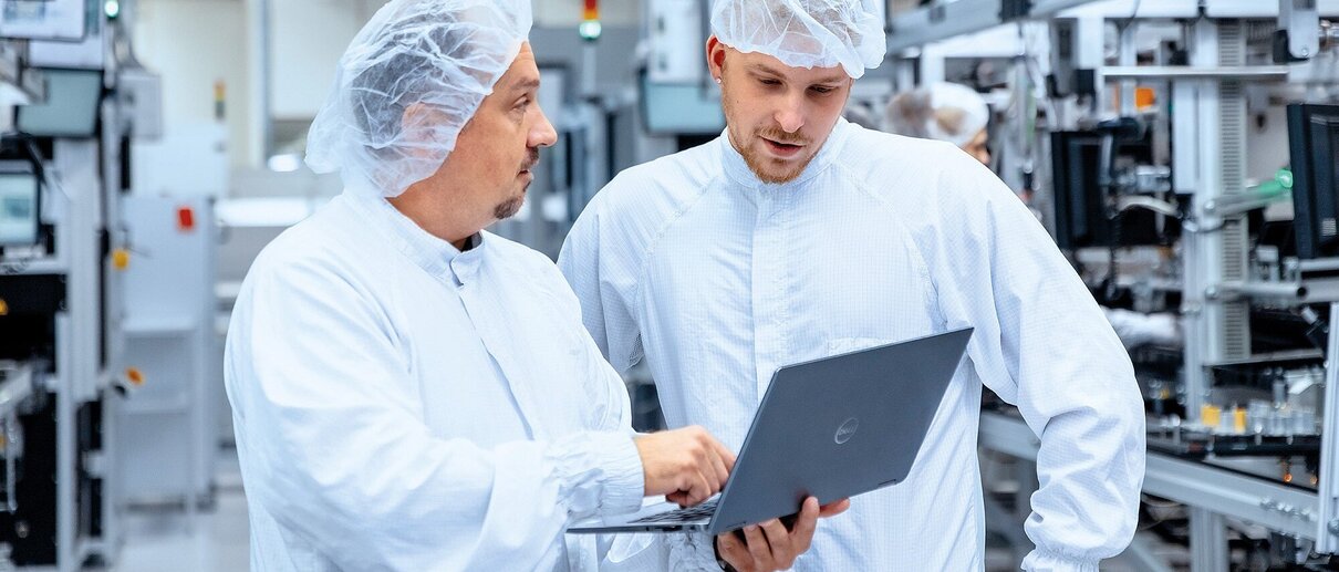 Zwei Mitarbeiter mit Reinraum-Sicherheitsausrüstung besprechen Abläufe. 