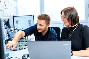 Zwei Mitarbeiter arbeiten an Elektronikentwicklung und Simulationen am Computer.