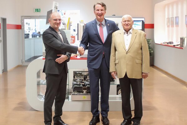 Herr Zollner Manfred steht mit zwei weiteren Personen in einem Raum mit Ausstellungsstücken; Die Männer geben sich die Hand