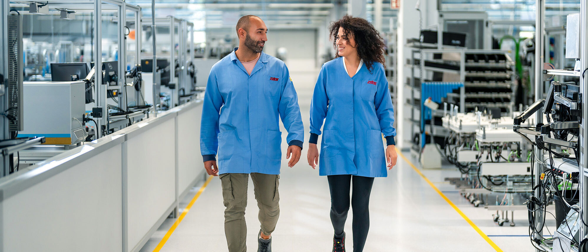 Mitarbeiter der Zollner Elektronik AG gehen durch die Fertigungshalle in ESD-Schutzbekleidung, Hinweis auf vielfältige Karriere- und Entwicklungsmöglichkeiten im Unternehmen.