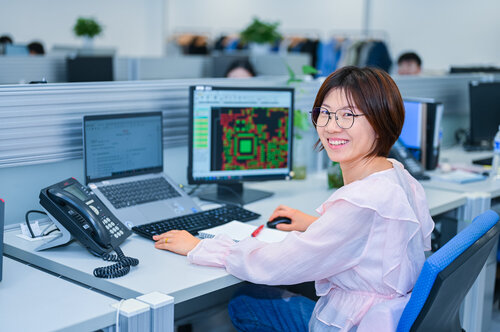 Mitarbeiterin lächelt während sie im Bürogebäude in China sitzt und arbeitet