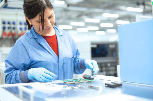 Produktionsmitarbeiterin schaut sich in der Produktion eine Platine an 